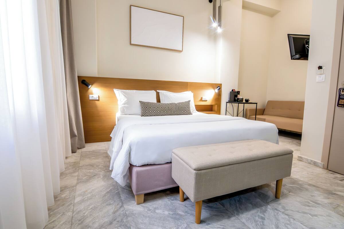 A modern hotel room with a bed, bedside tables, a bench, and a TV mounted on the wall.
