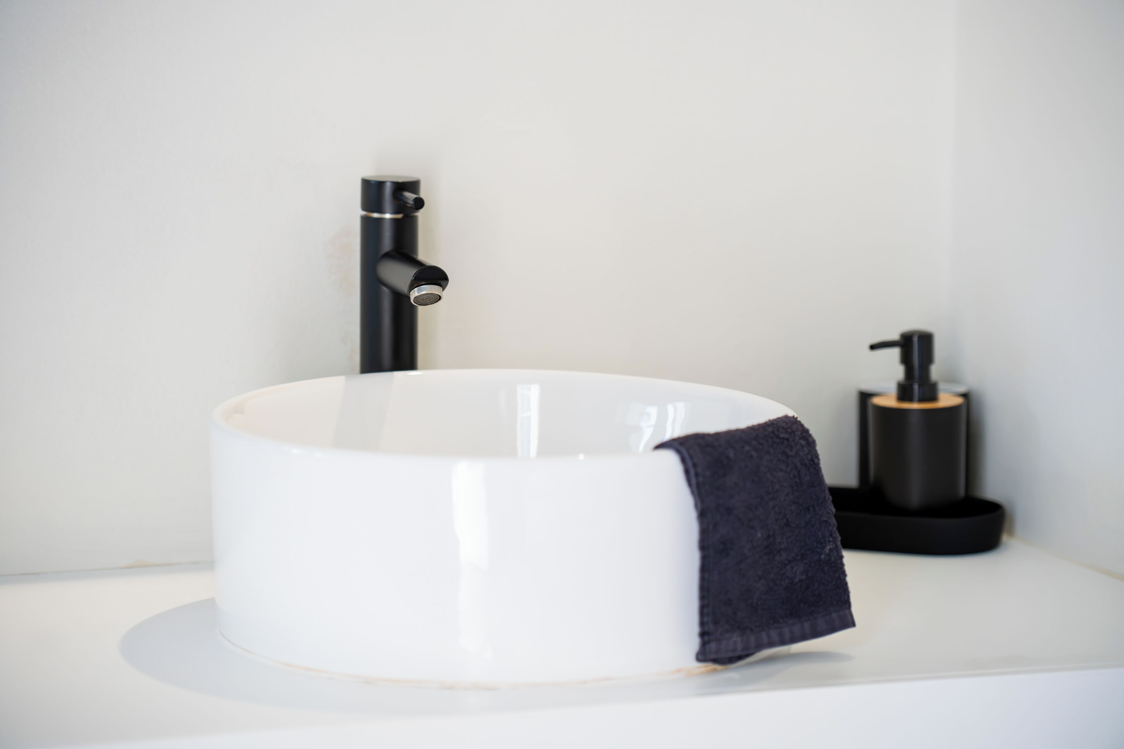 Un évier blanc avec un robinet noir et un distributeur de savon, le tout posé sur un plan de travail blanc.