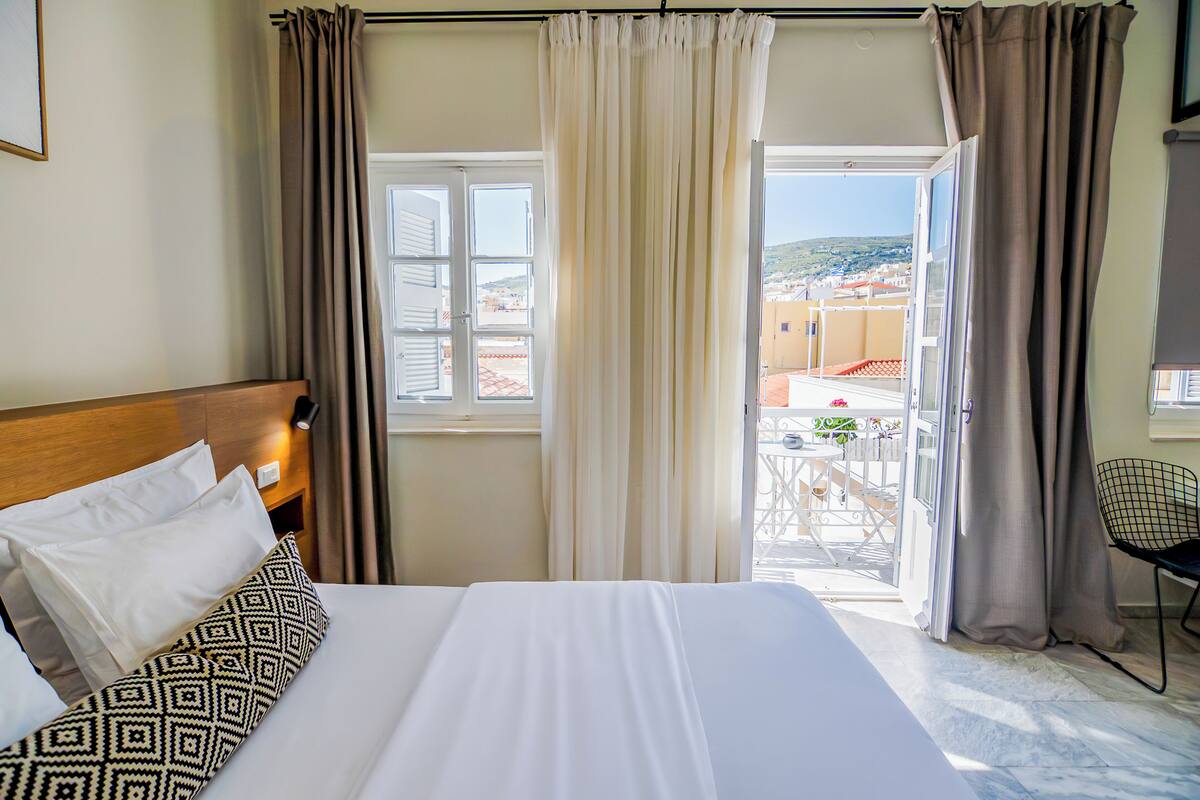 A hotel room with a bed, curtains, a window with a view, and a chair.