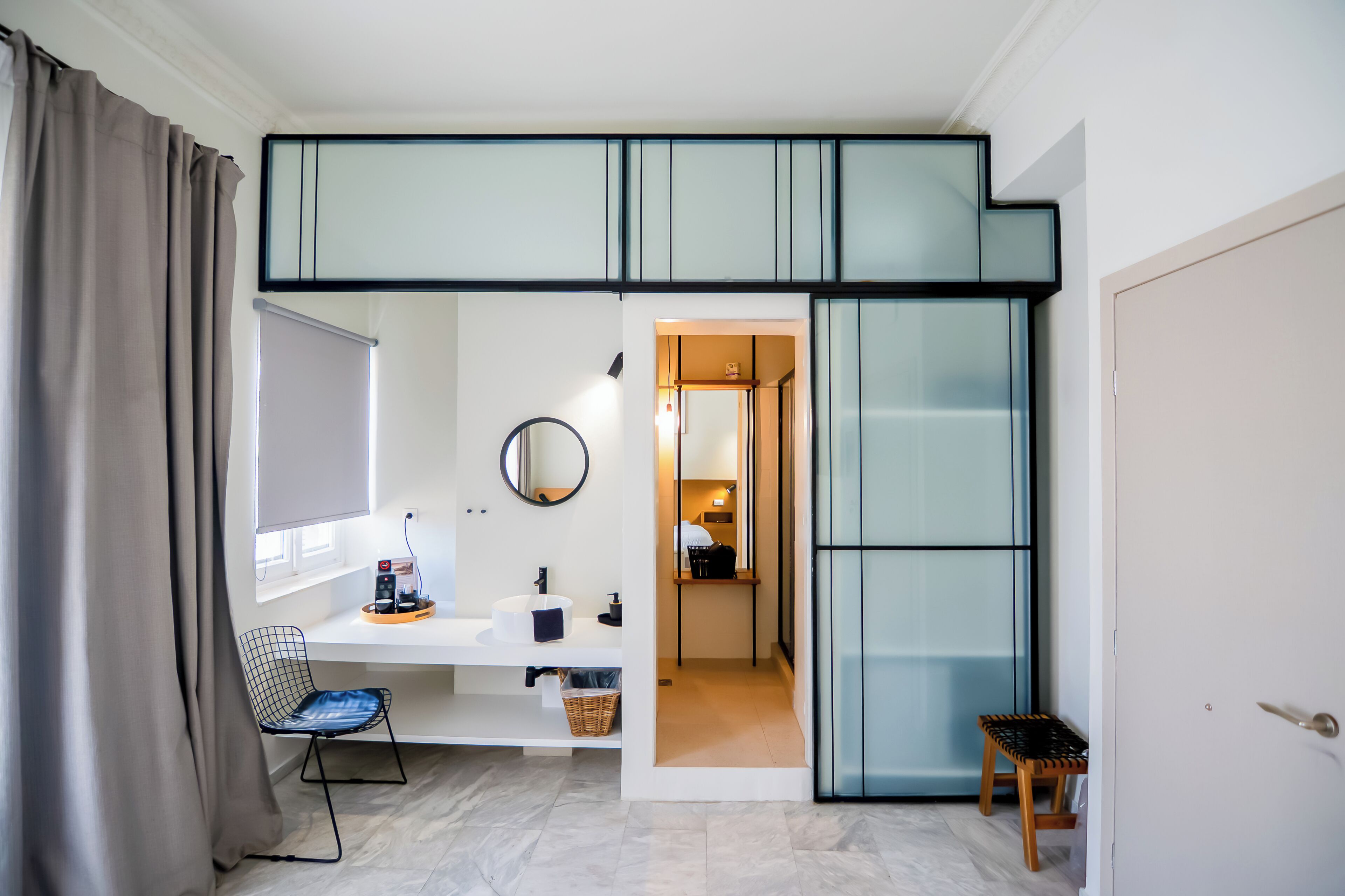A compact room with a bed, a desk, a chair, and a small stool.