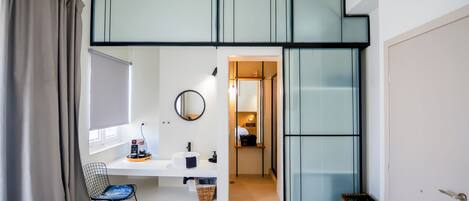 A compact room with a bed, a desk, a chair, and a small stool.