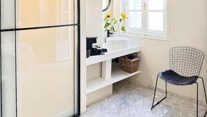 Une salle de bain avec un meuble-lavabo blanc, un miroir, un évier et une chaise.