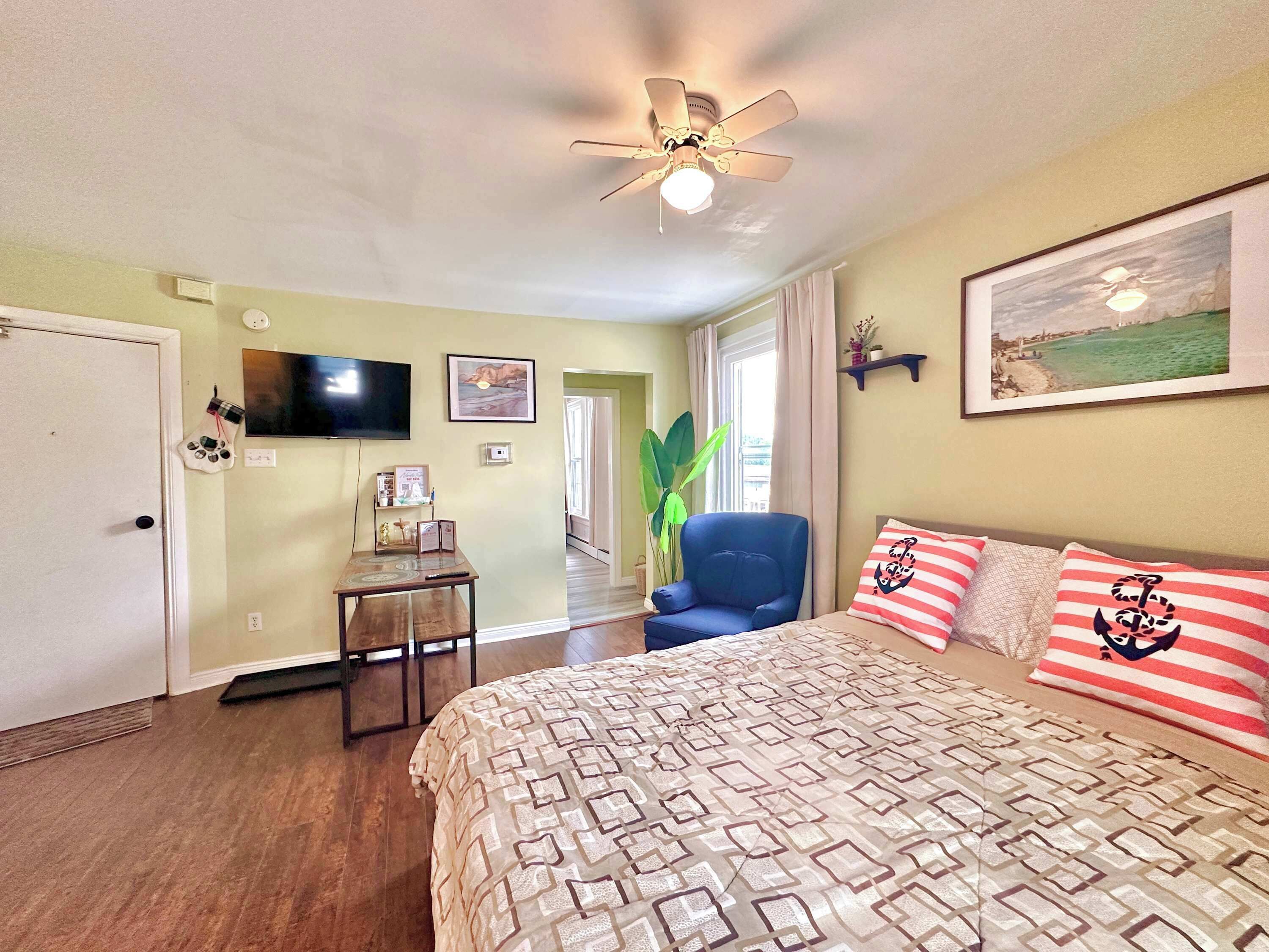 A bedroom with a bed, a chair, a television, and a ceiling fan.