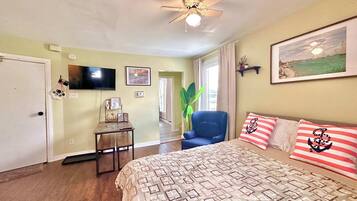 A bedroom with a bed, a chair, a television, and a ceiling fan.