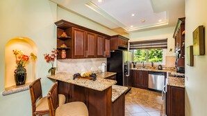 Una cucina moderna con mobili in legno scuro, piani in granito ed elettrodomestici in acciaio inossidabile. C'è un'area pranzo con sedie in vimini e un vaso con fiori.
