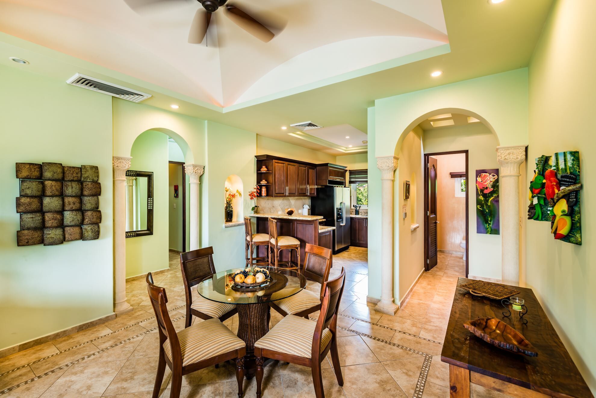 A spacious dining area with a round table and chairs, a kitchen in the background, and a hallway leading to other rooms.