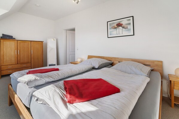 A bedroom with a bed, wooden wardrobe, and a door leading to another room.