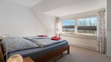 Ein Schlafzimmer mit einem Bett, einem Nachttisch mit Lampe, einem Fenster mit Vorhängen und einer Heizung.
