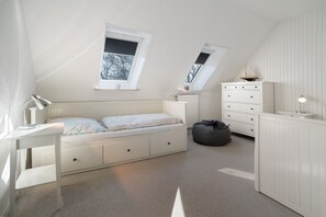Un dormitorio con cama elevada, escritorio, cómoda y ventana con vista a árboles.