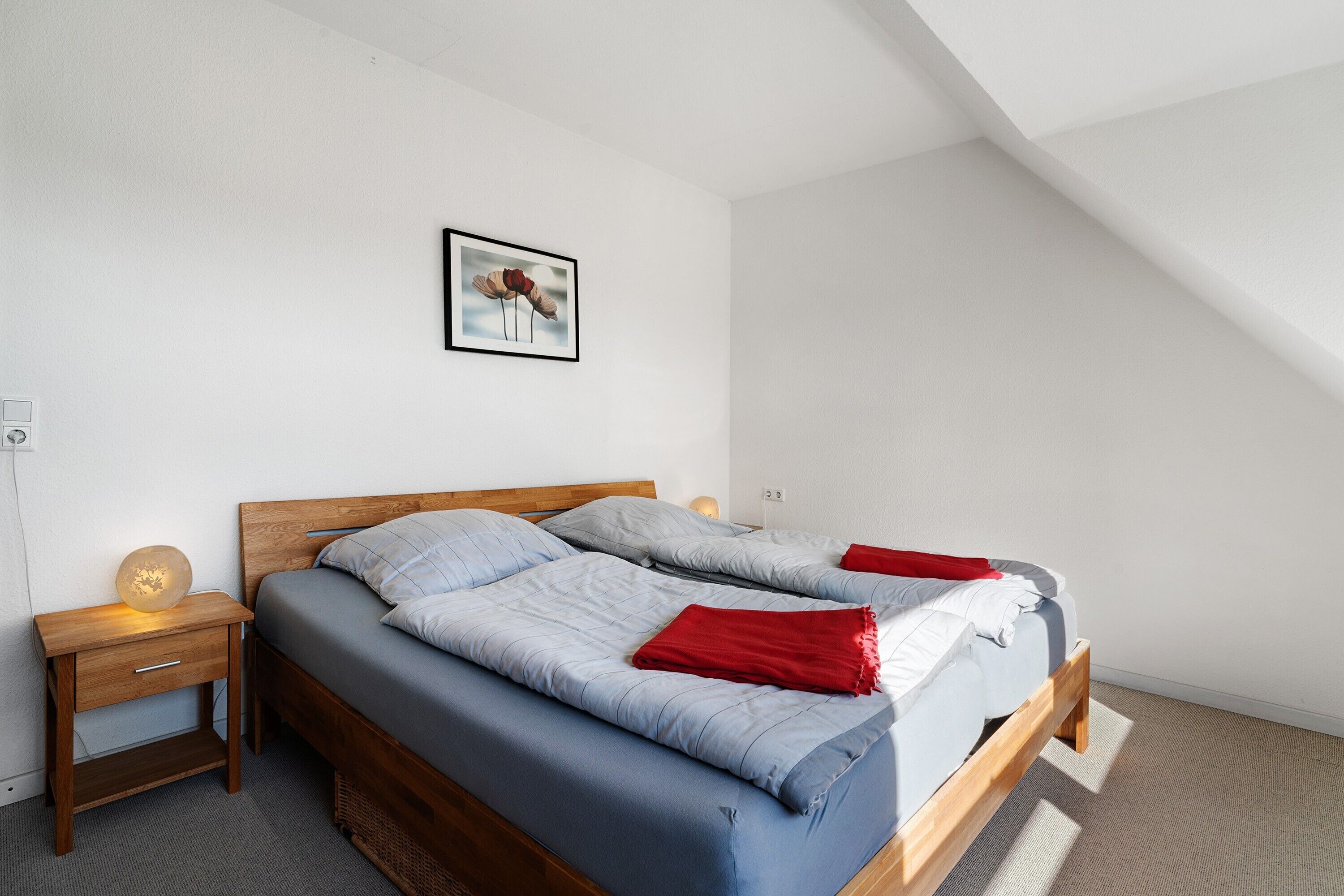 A bedroom with a wooden bed, a nightstand, a wall-mounted lamp, and a framed picture.