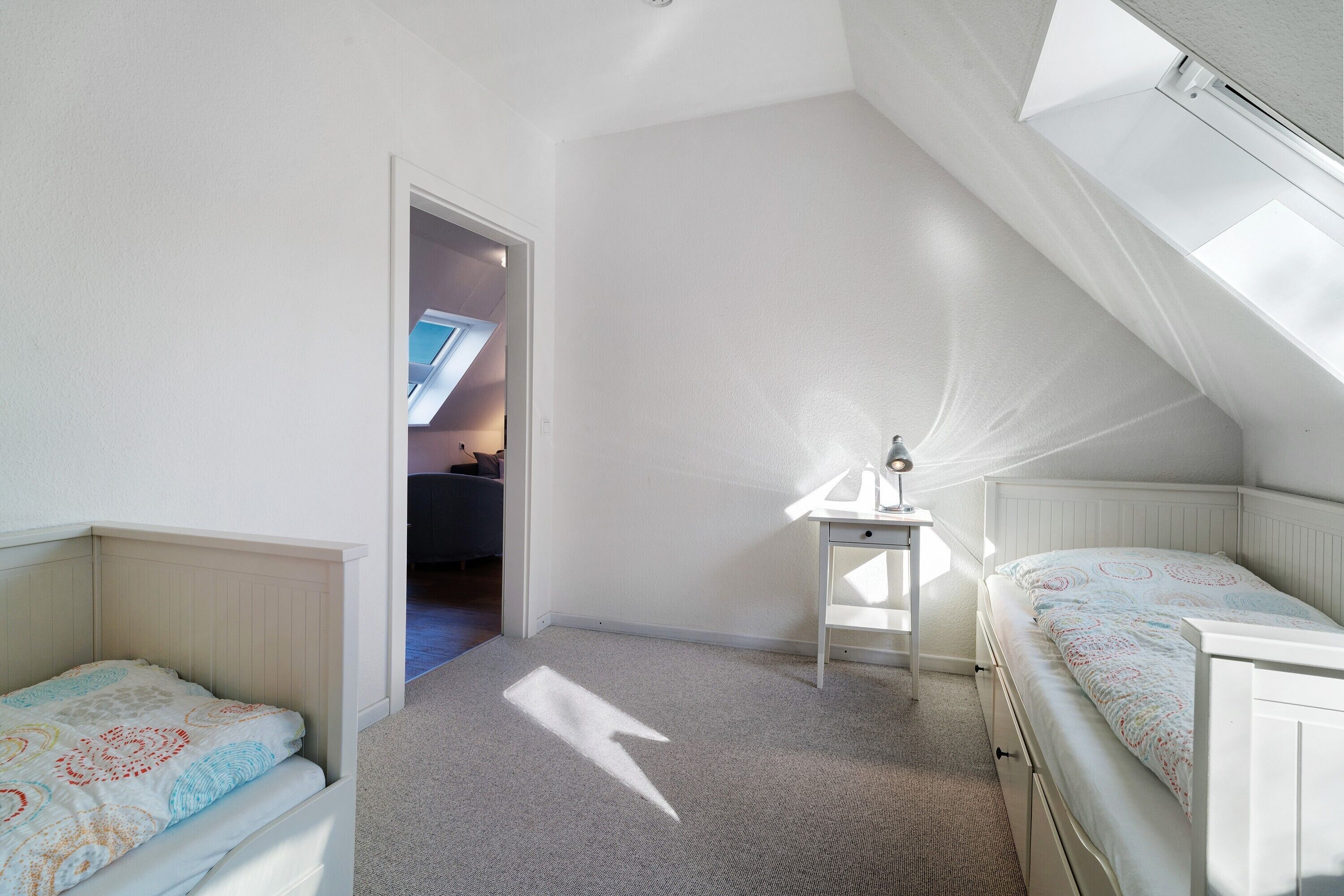 A bedroom with a sloped ceiling, a skylight, a bed, a desk, and a chair.