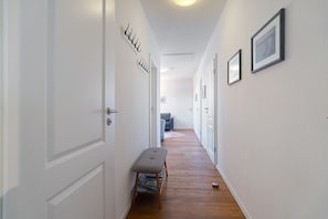 A hallway with white walls, wooden flooring, a bench, and framed pictures.