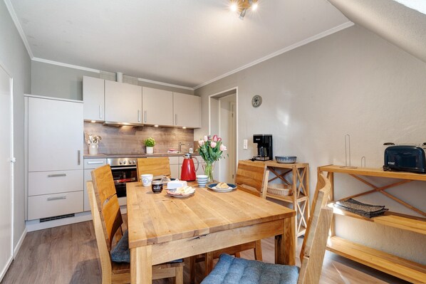 Una cocina moderna con armarios blancos, una mesa de comedor de madera y una cafetera.