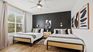 Ein Schlafzimmer mit zwei Betten, einem Deckenventilator, Kunstwerken an den Wänden und einem Fenster mit Vorhängen.