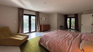 Ein modernes Schlafzimmer mit einem großen Bett, einer Couch und einer Kommode. Eine Glastür führt auf einen Balkon.