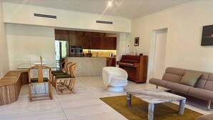 Ein modernes Wohnzimmer mit Küche im Hintergrund, einer Essecke mit rundem Tisch und Stühlen sowie einem Sofa und einem braunen Teppich.