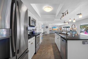 A modern kitchen with stainless steel appliances, a central island, pendant lighting, and a view to the outside. - Saltwater Pool Beach Home (Largo)