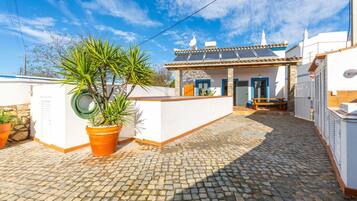 A courtyard with cobblestone flooring, a potted plant, and a building with a tiled roof and white walls.