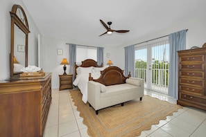 A bedroom with a bed, dresser, mirror, ceiling fan, and large windows. - Exclusive White Marlin Beach Retreat - Private Beach Access & Dock (Islamorada)
