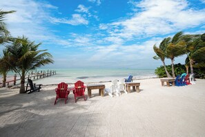 A beach with chairs and tables, palm trees, and a wooden walkway. - Exclusive White Marlin Beach Retreat - Private Beach Access & Dock (Islamorada)