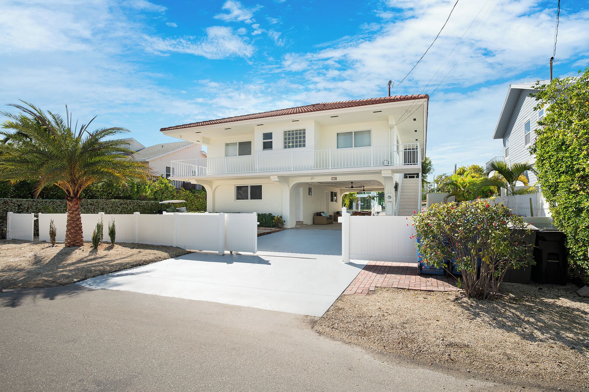 A two-story house with a balcony, a driveway, and a white fence.