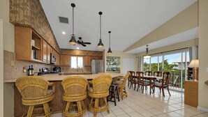 A spacious kitchen with a central island, bar stools, and a dining area with chairs. - Exclusive White Marlin Beach Retreat - Private Beach Access & Dock (Islamorada)