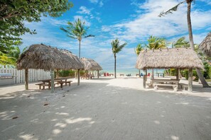 A beach with thatched-roof structures, wooden benches, and palm trees. - Exclusive White Marlin Beach Retreat - Private Beach Access & Dock (Islamorada)