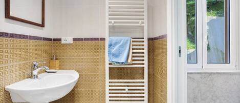 A bathroom with a white sink, a towel rack, and a window with a view of greenery.