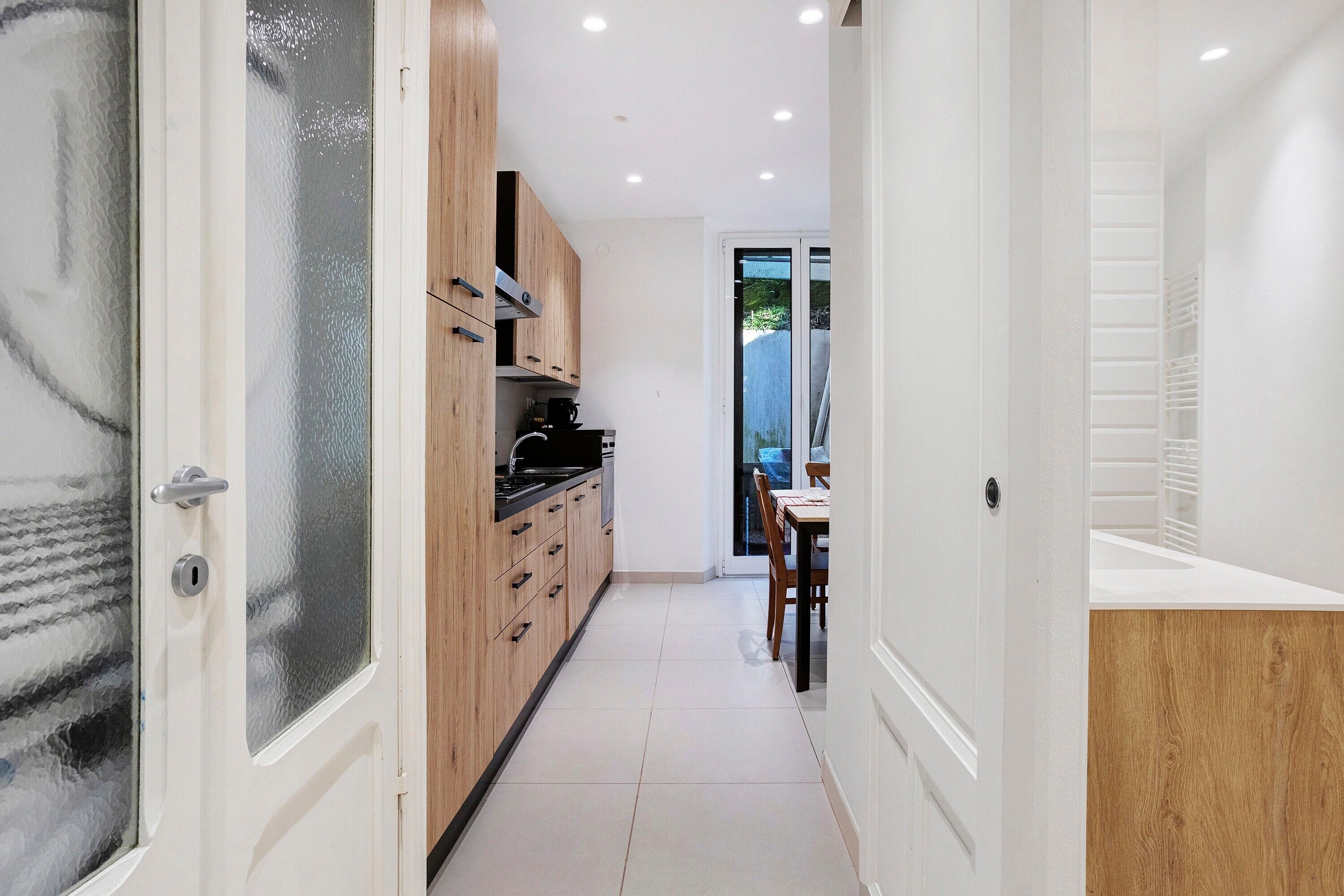 A narrow hallway with wooden cabinets, a kitchen area, and a dining table.