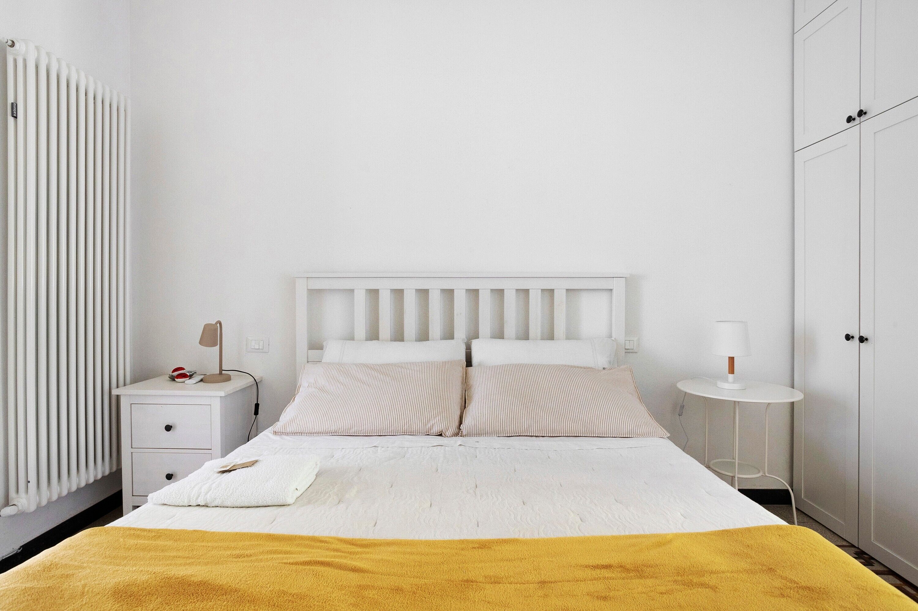 Un dormitorio con cama, mesitas de noche, un radiador y un armario.