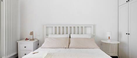 Un dormitorio con cama, mesitas de noche, un radiador y un armario.
