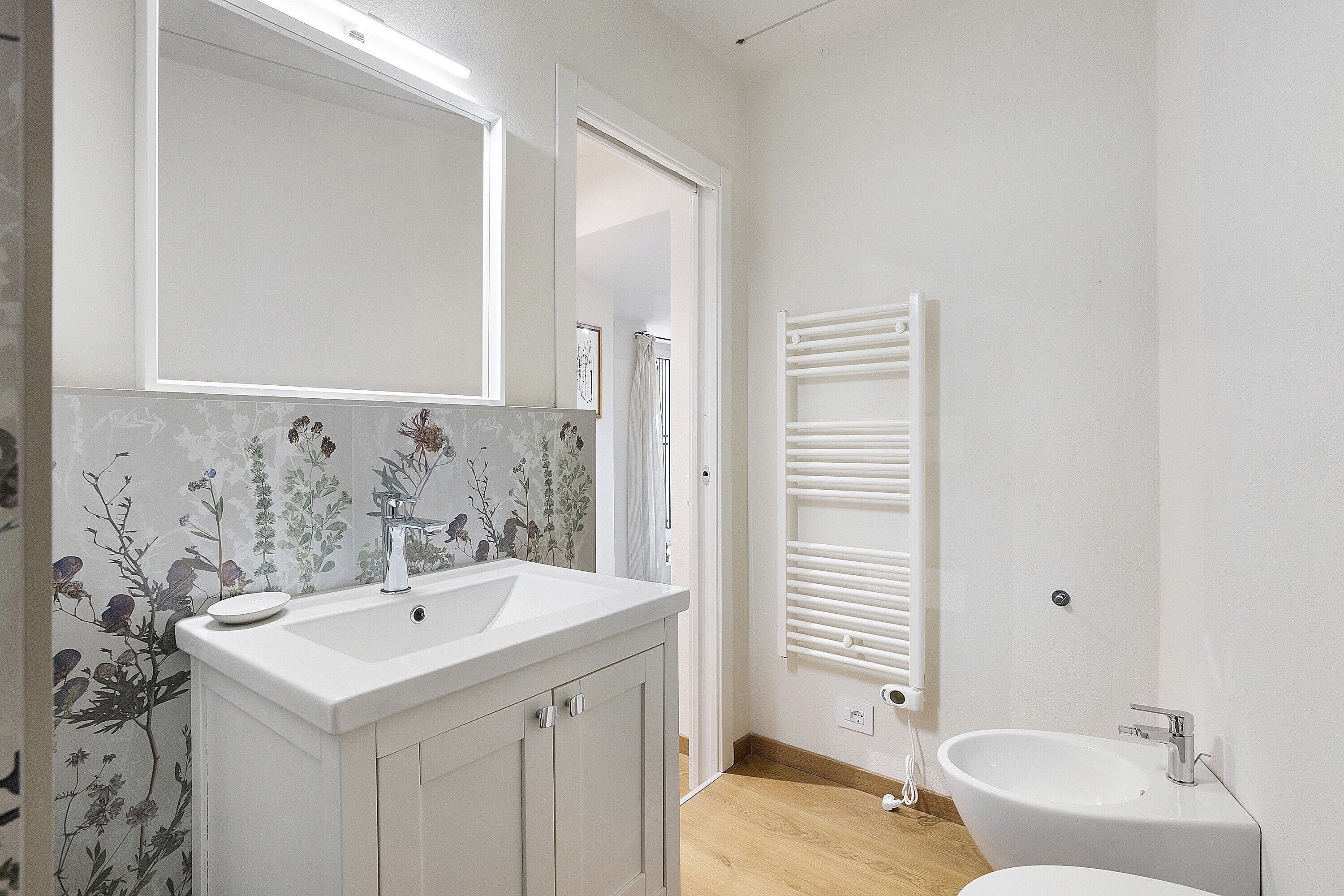 Un baño con lavamanos blanco, espejo y zona de ducha.