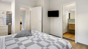Ett sovrum med en säng, en tv som är monterad på väggen och ett badrum som syns genom en öppen dörr.
