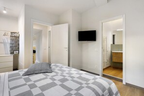 A bedroom with a bed, a TV mounted on the wall, and a bathroom visible through an open door. - 'Loft Fossati' Apartment with Wi-Fi and Air Conditioning (La Spezia)