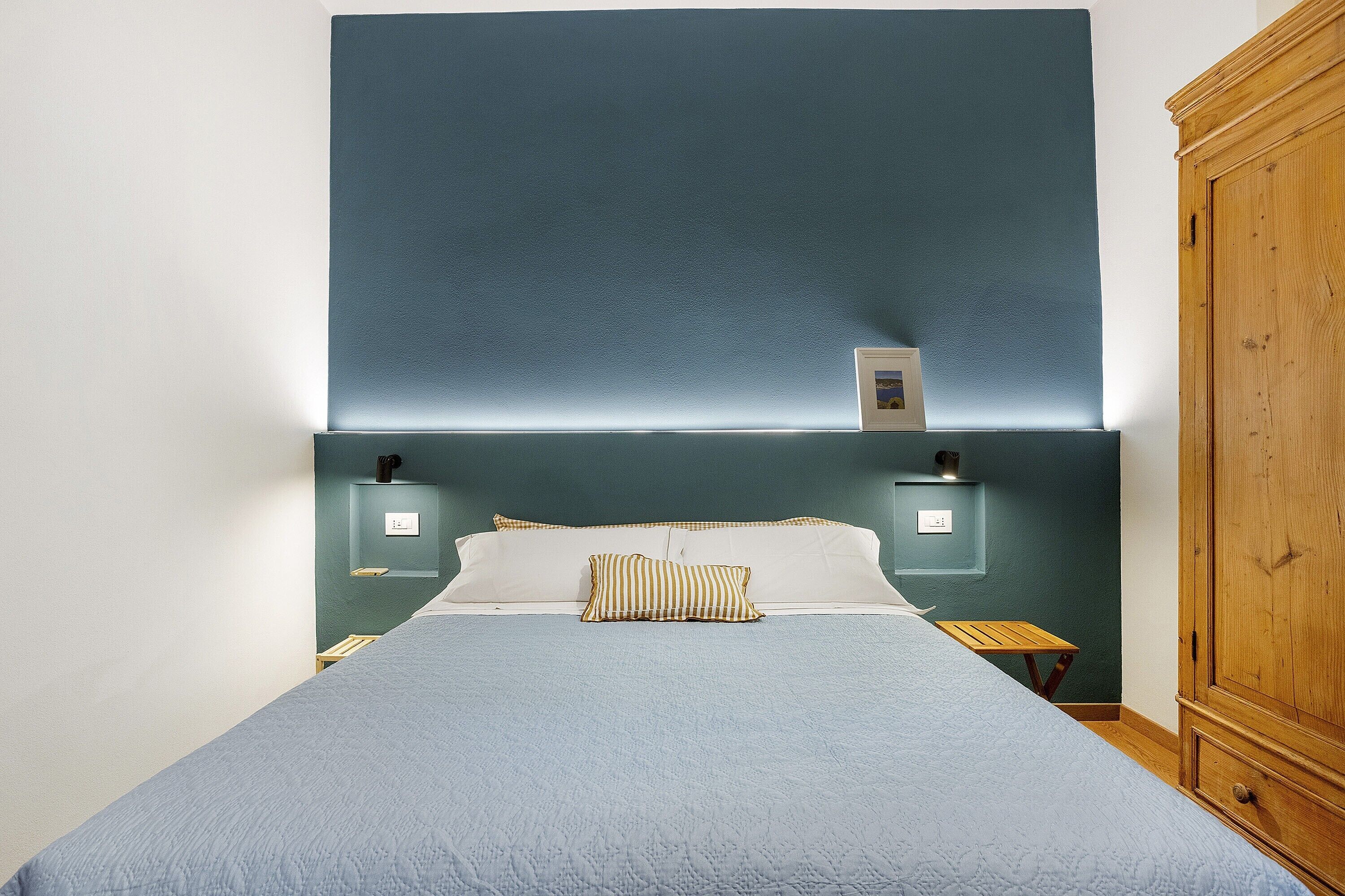 Un lit avec une couette bleue, un oreiller à rayures et deux tables de chevet avec des lampes.