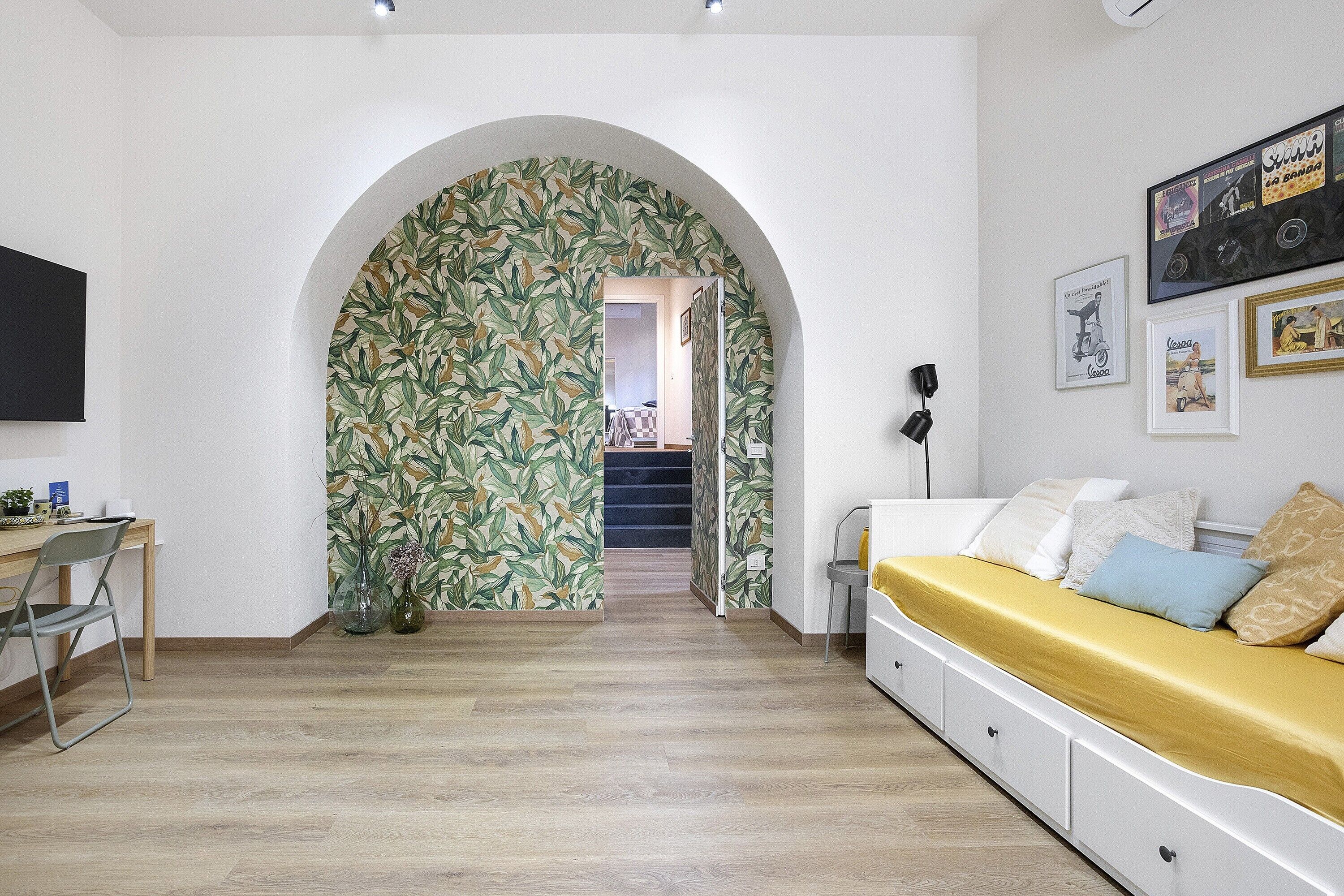 Ein Zimmer mit Holzboden, einem Schreibtisch mit Stuhl, einer Couch mit Kissen, einem Fernseher und einer Wand mit gerahmten Bildern.