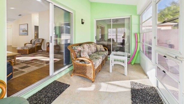 A spacious living area with a large sliding glass door, a ceiling fan, and a wicker sofa. - Cozy Courtyard Villa with Pool in De La Vista (The Villages)