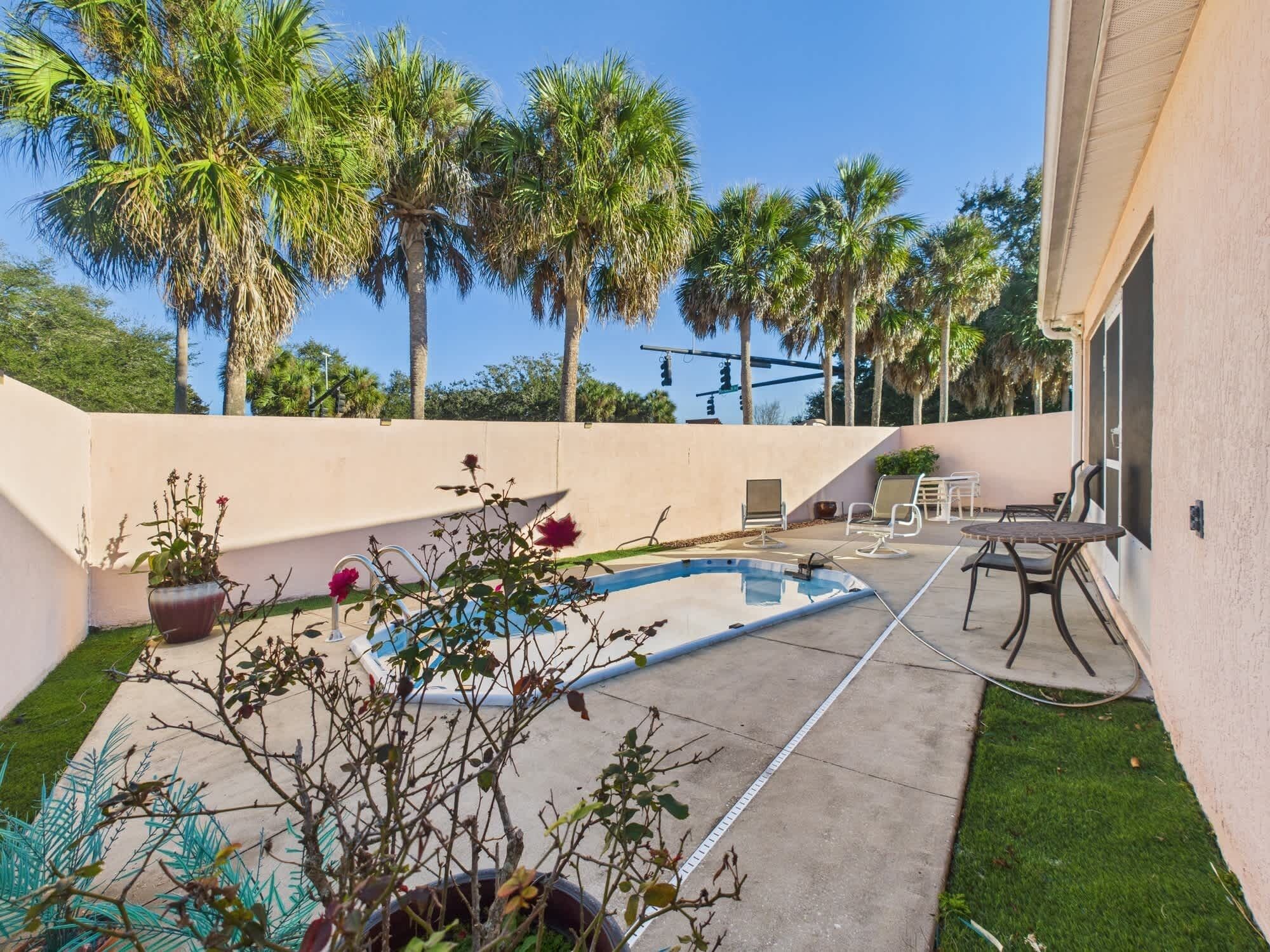 A backyard with a swimming pool, outdoor furniture, and palm trees.