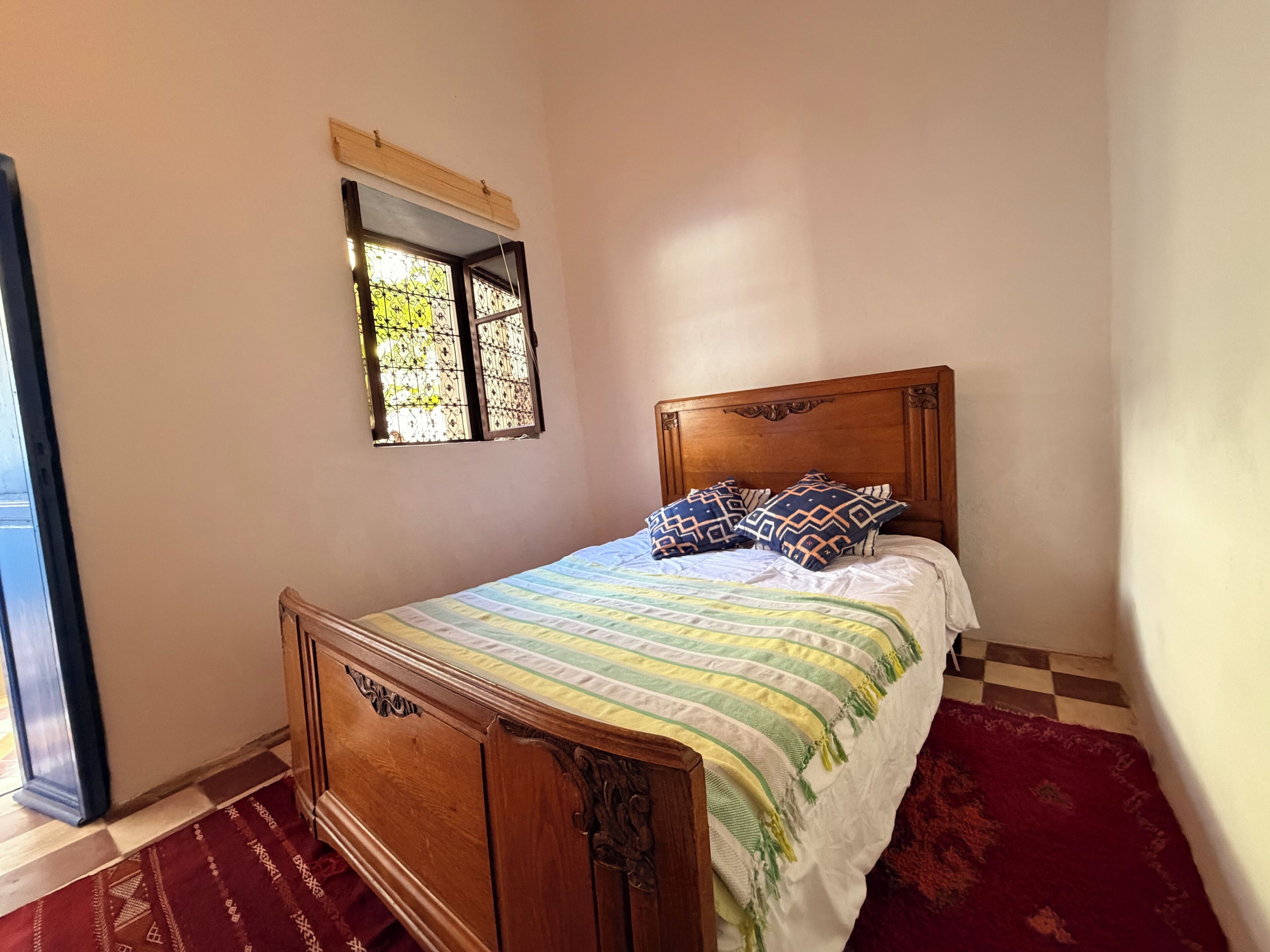 Une chambre à coucher avec un lit en bois, une literie à motifs, une petite fenêtre et un tapis rouge.