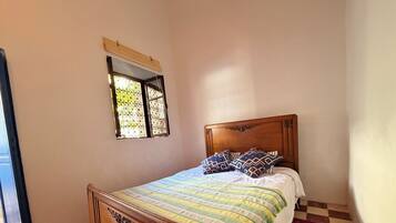 Une chambre à coucher avec un lit en bois, une literie à motifs, une petite fenêtre et un tapis rouge.