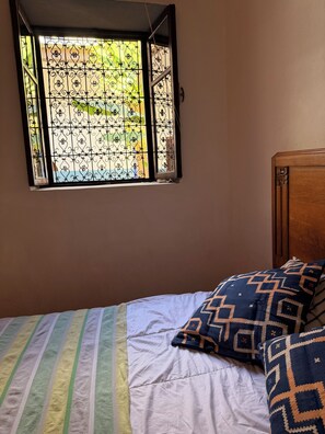 A bed with striped bedding and patterned pillows, a wooden headboard, and a window with decorative iron bars.