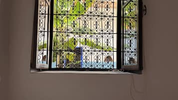 Ein Fenster mit schmiedeeisernen Ziergittern, ein Bett mit gemusterten Betttextilien und eine Wandleuchte.
