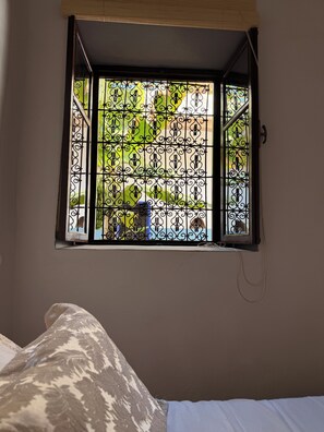 A window with decorative iron bars, a bed with patterned bedding, and a wall-mounted light fixture.