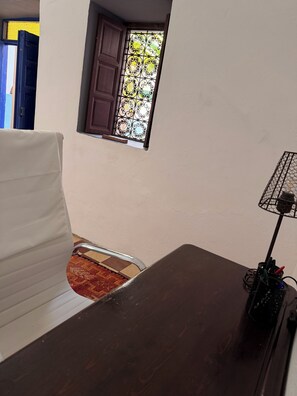A room with a white sofa, a wooden table, a small window with decorative iron bars, and a floor lamp.