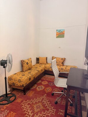 A small room with a bed, a desk, a chair, and a standing fan.