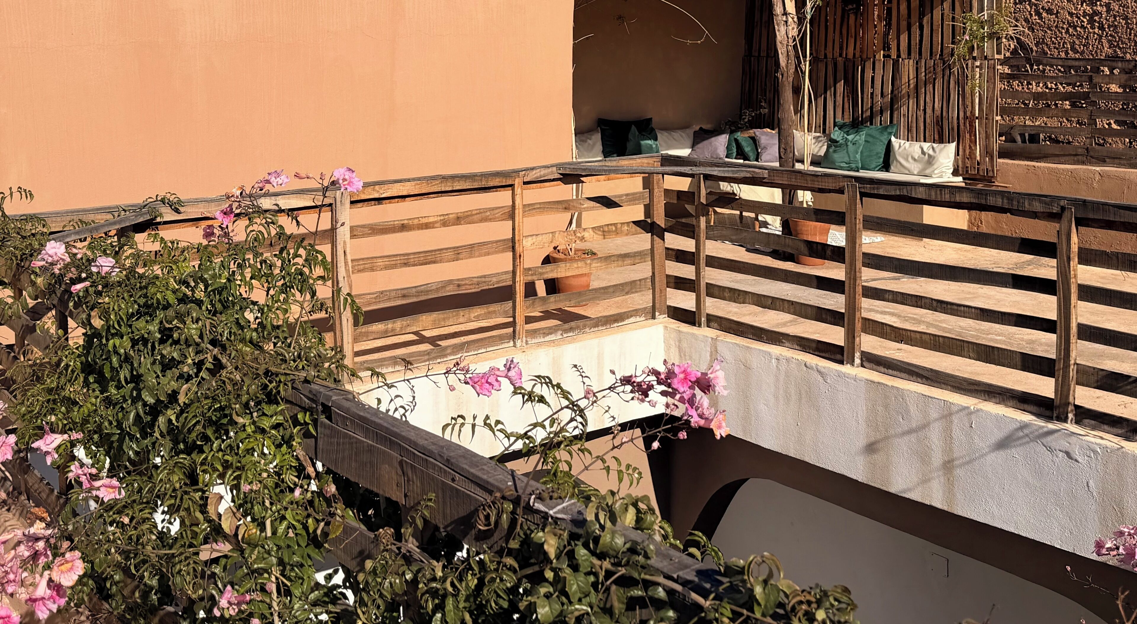 Un balcon avec une balustrade en bois, un petit coin salon avec des coussins et des plantes en pot.