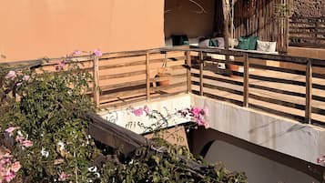 A balcony with a wooden railing, a small seating area with cushions, and potted plants.