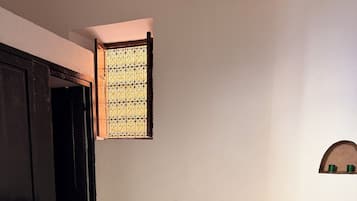 Ein Zimmer mit einem Holzschaukelstuhl, einem gemusterten Teppich, einer kleinen Ablage mit zwei grünen Tassen und einem Fenster mit dekorativen Eisenstreben.