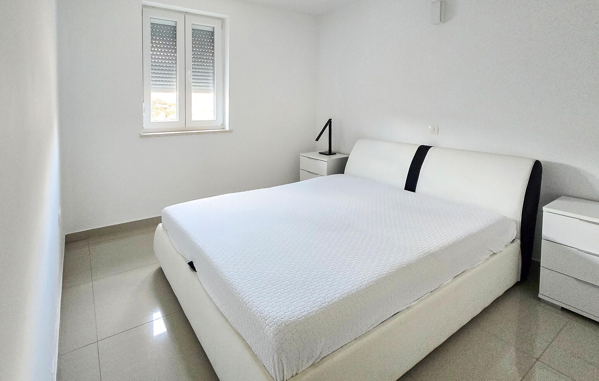 A bedroom with a bed, a nightstand, a lamp, and a window.