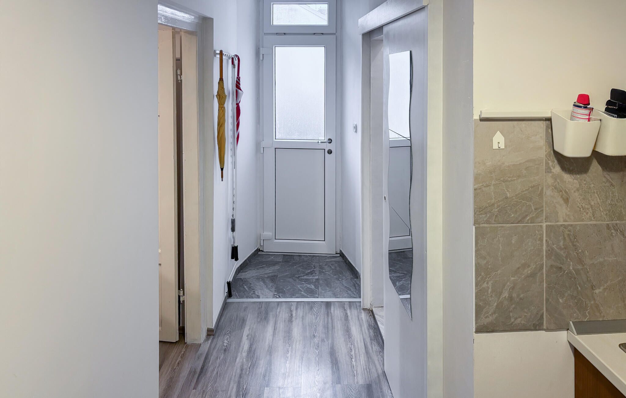 Un couloir étroit avec une porte au fond, un mur recouvert de carreaux et muni d’un distributeur de serviettes, et un plancher en bois.